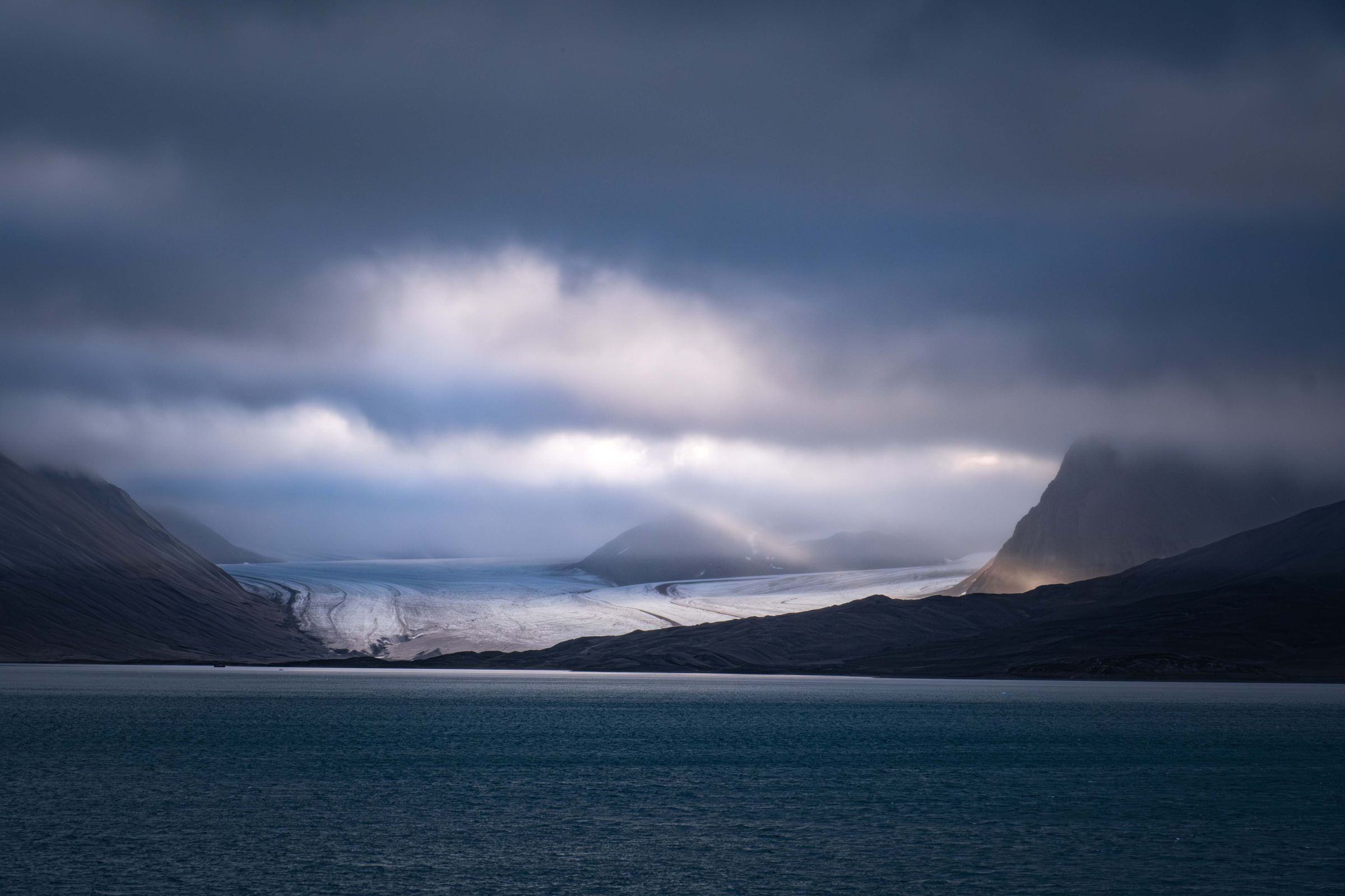 A glacier meeting dark Arctic water in Svalbard under heavy clouds